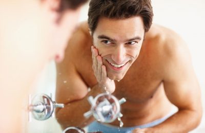 Smiling young man washing his face at the basin