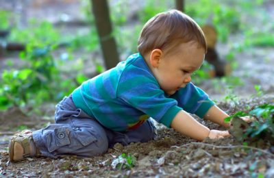 cute baby boy digging the ground in spring forest