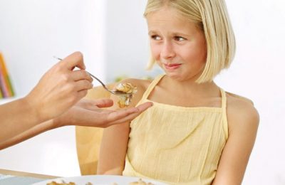 Mother's Hand Feeding Food to a Young Girl (13-14) Who Is Making a Face --- Image by © Royalty-Free/Corbis