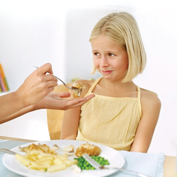 Mother's Hand Feeding Food to a Young Girl (13-14) Who Is Making a Face --- Image by © Royalty-Free/Corbis