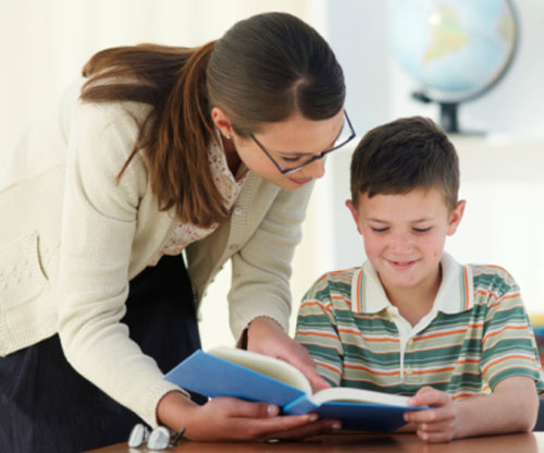 Teacher helping boy (8-9) with work in classroom