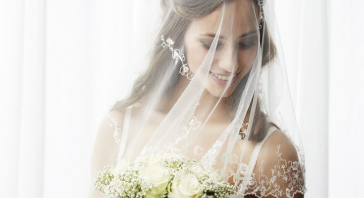Excited young bride in veil holding bouquet