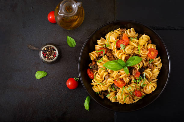 Pasta Fusilli  with tomatoes, beef and basil in black bowl on table. Top view. Flat lay